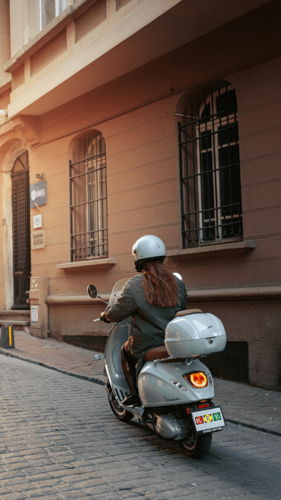 Frau, die auf einer mintgrünen Vespa sitzt und über ein Kopfsteinpflaster fährt.